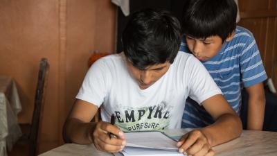 Two boys hunches over a book reading 